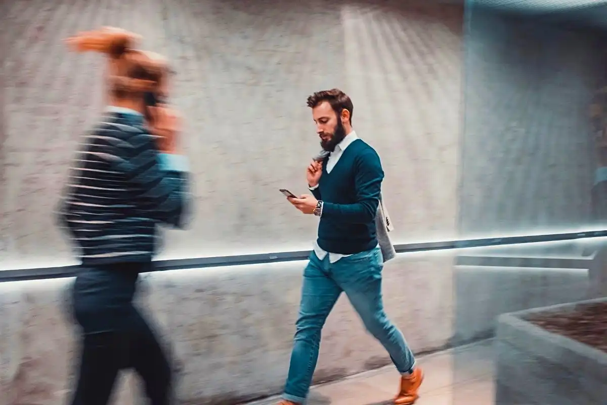 Man walking while looking down at his mobile phone - Happy Mind Training Blog | Why People Thrive in Coworking Spaces