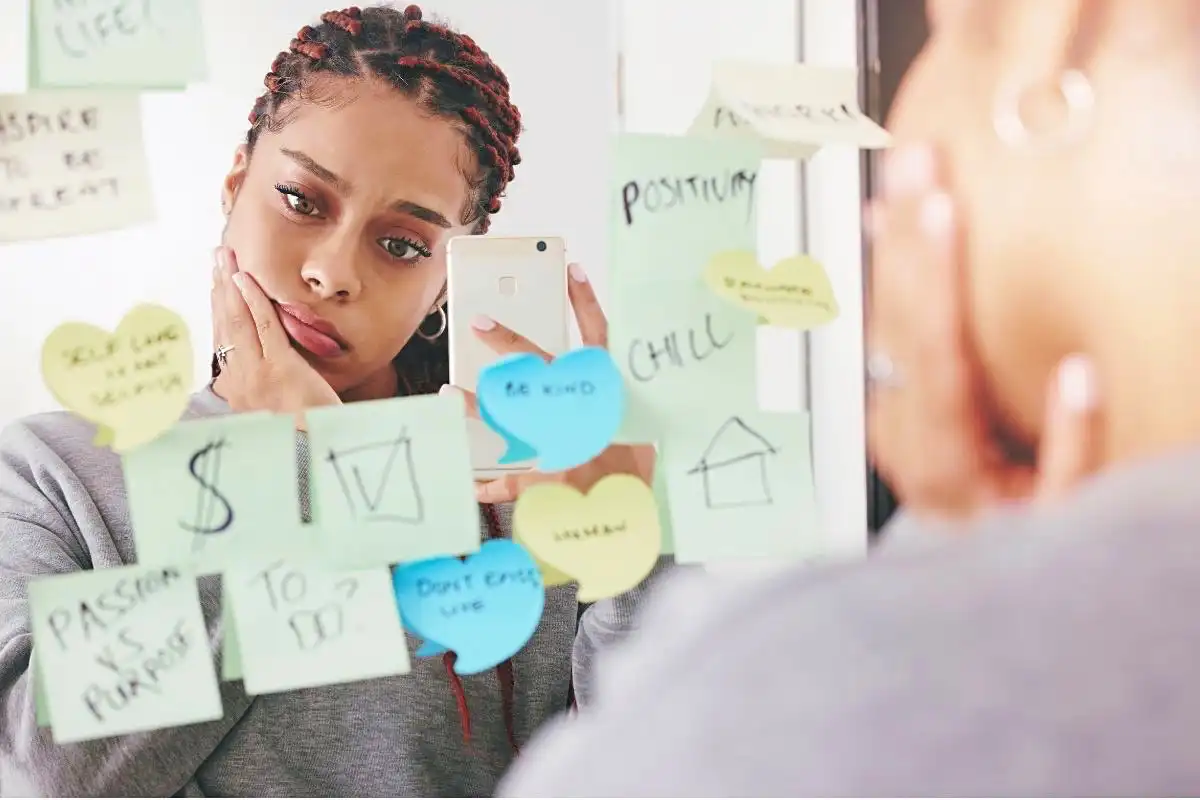 Woman with a worried look staring at a mirror full of sticky notes - Happy Mind Training Blog | Nine Ways to Combat Negative Self-talk