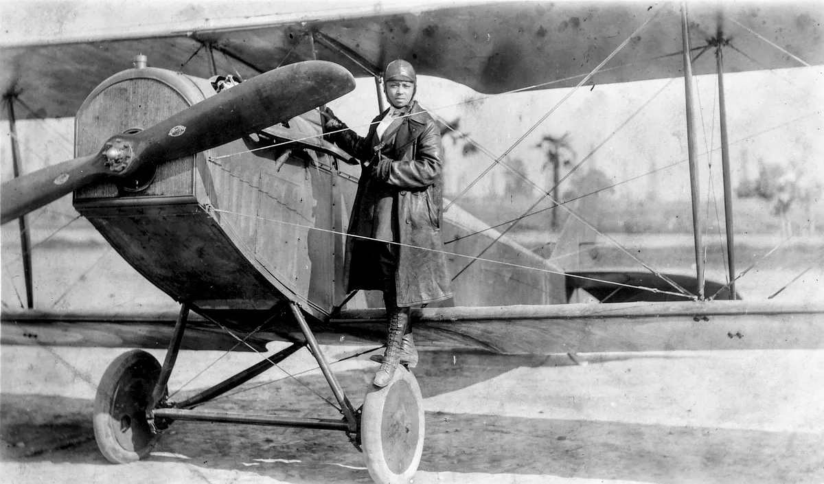 B&W image of a woman pilot stood on the wheel of her plane