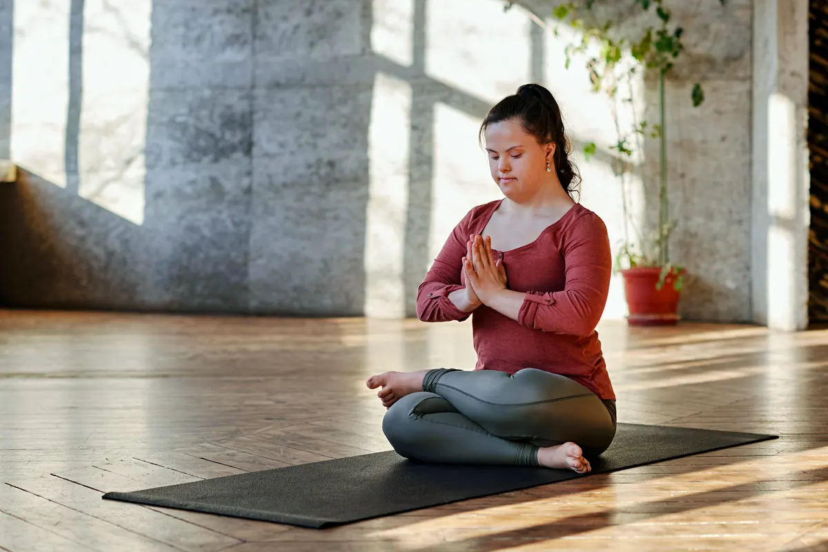A young woman with Down syndrome sitting on the floor in a yoga pose
