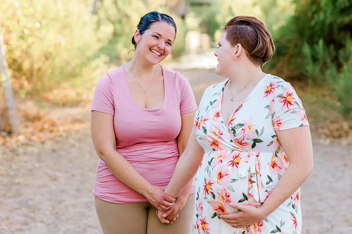Two women in love smiling at each other and one woman is pregnant.
