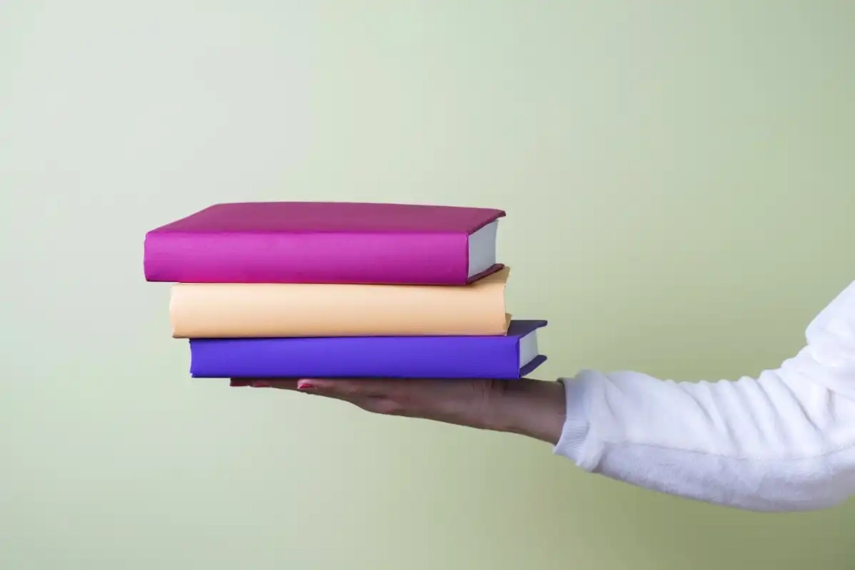 Arm holding three books - Happy Mind Training Blog | Language Can Shape Our Reality