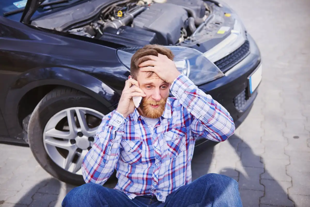 Man on his mobile phone looking frustrated sitting next to a broken down car - HappyMind Training Blog | Pouring From an Empty Cup